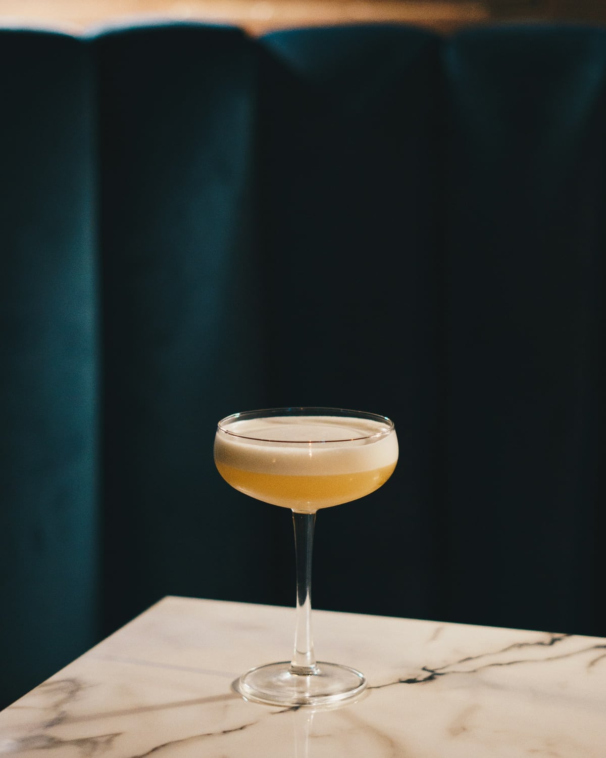 Cocktail en copa coupe sobre una mesa de mármol, con un sillón verde de fondo