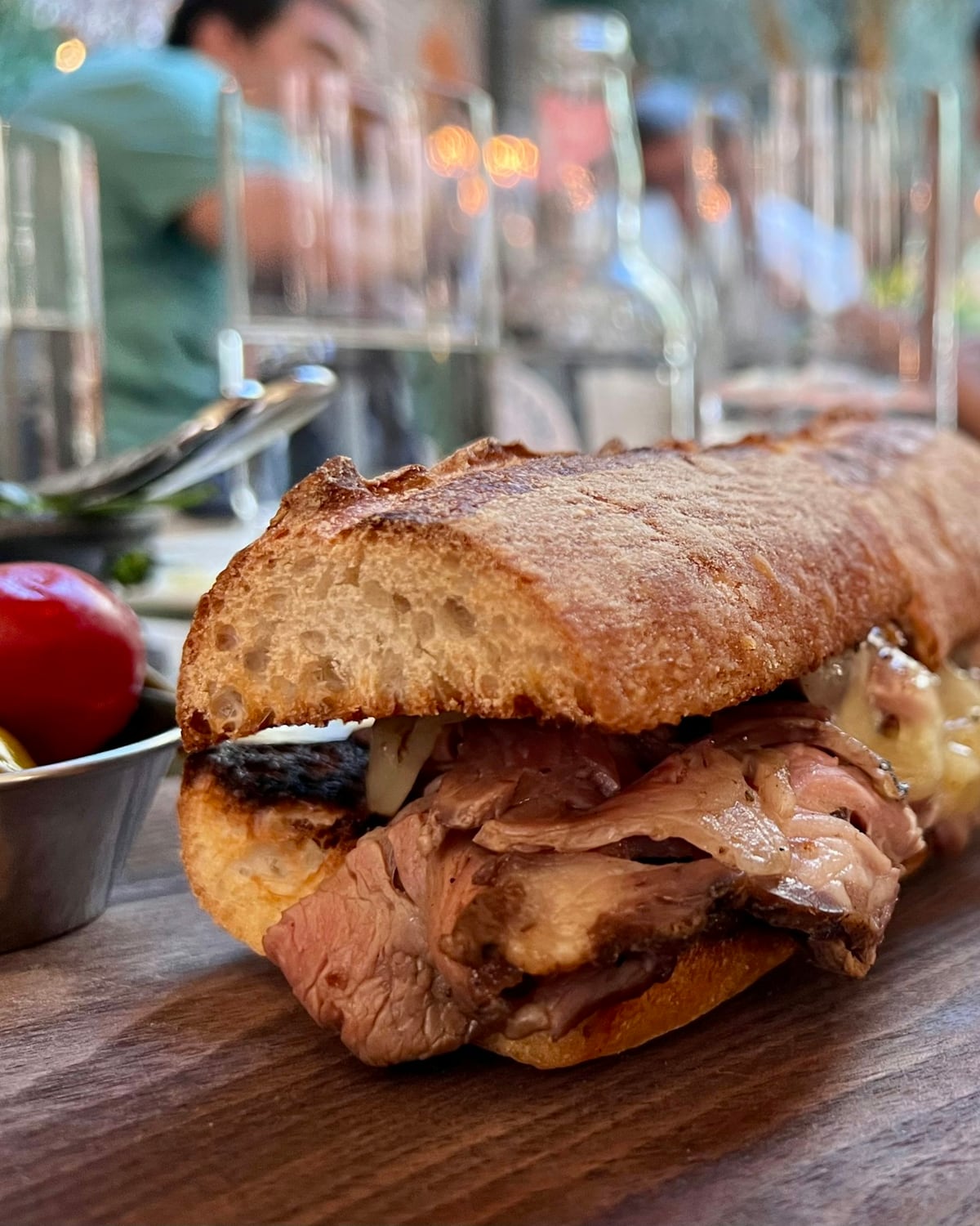 Sándwich de carne asada con queso derretido en pan baguette sobre una tabla de madera