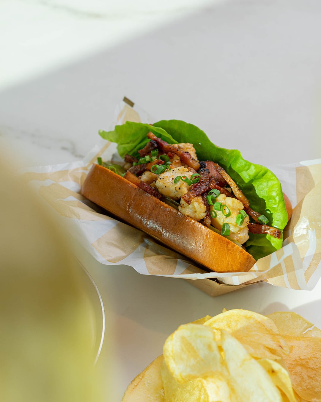 Lobster roll en pan brioche con lechuga, sobre papel, junto a papitas fritas